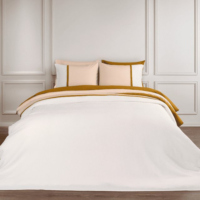 Dommelin Bari op een wit bed met een gekleurd randdetail op overtrek en kussenslopen.